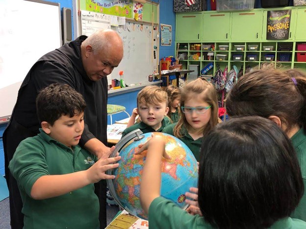 Father Hugo Lopez, OSB, Superintendent of Colegio San Benito, finding Guatemala on the globe with Christ the King students.